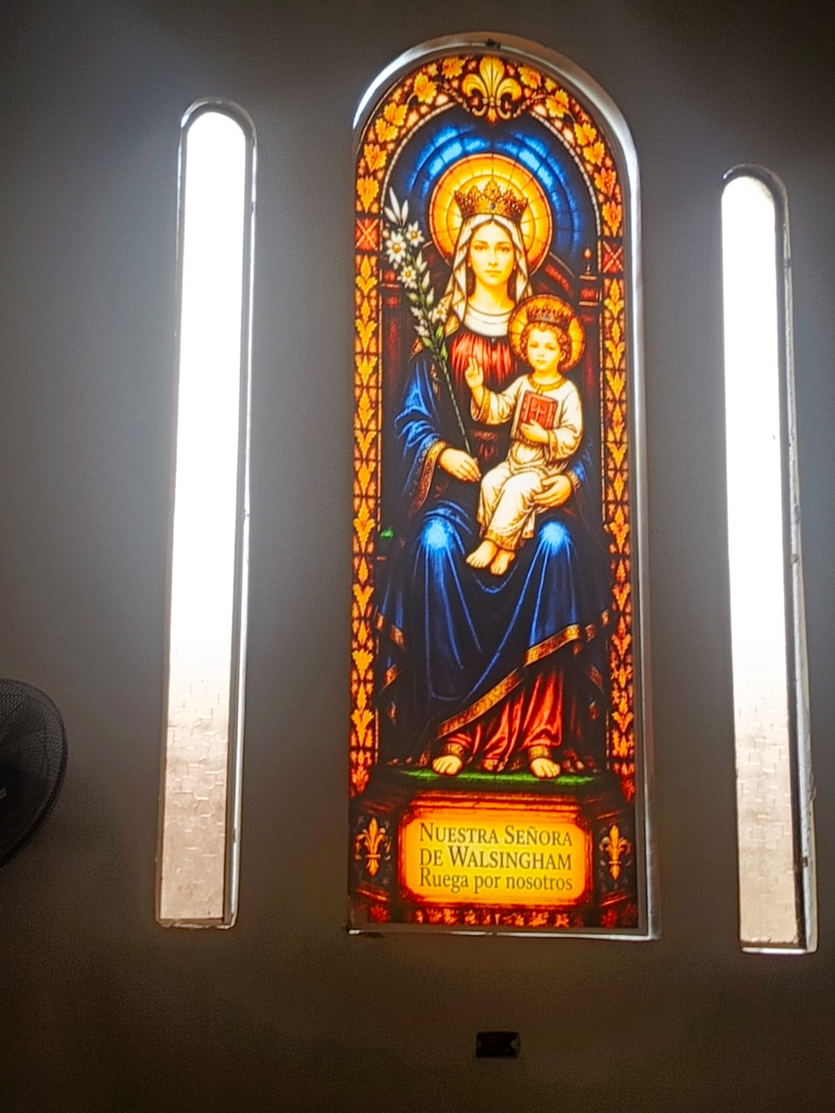 Vitral de Nuestra Señora de Walsingham con la Virgen María y el Niño Jesús coronados, con la inscripción Ruega por nosotros