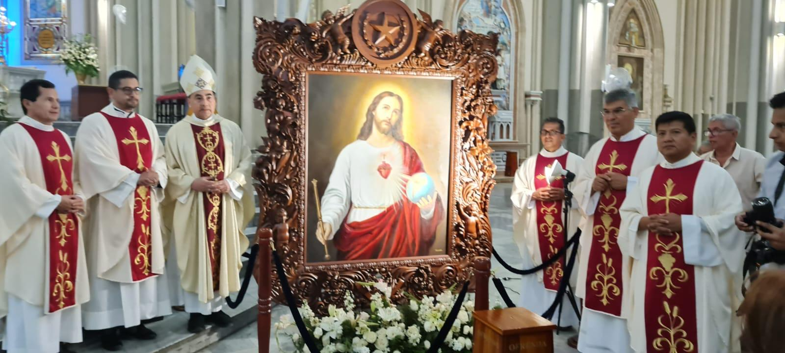 Pintura del Sagrado Corazón de Jesús en marco tallado, rodeada por sacerdotes en el interior de una iglesia